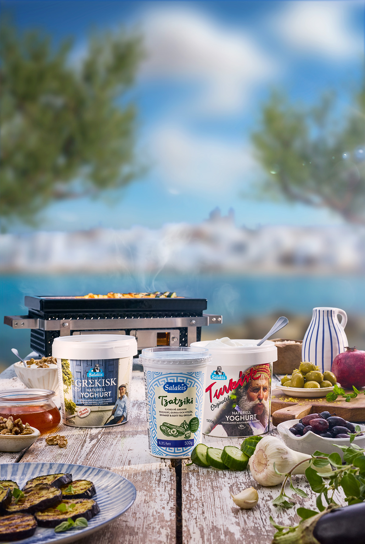 Medelhavsinspirerat bord med Salakis yoghurt och tzatziki, grillade grönsaker och färska råvaror vid havet i sommarsol.