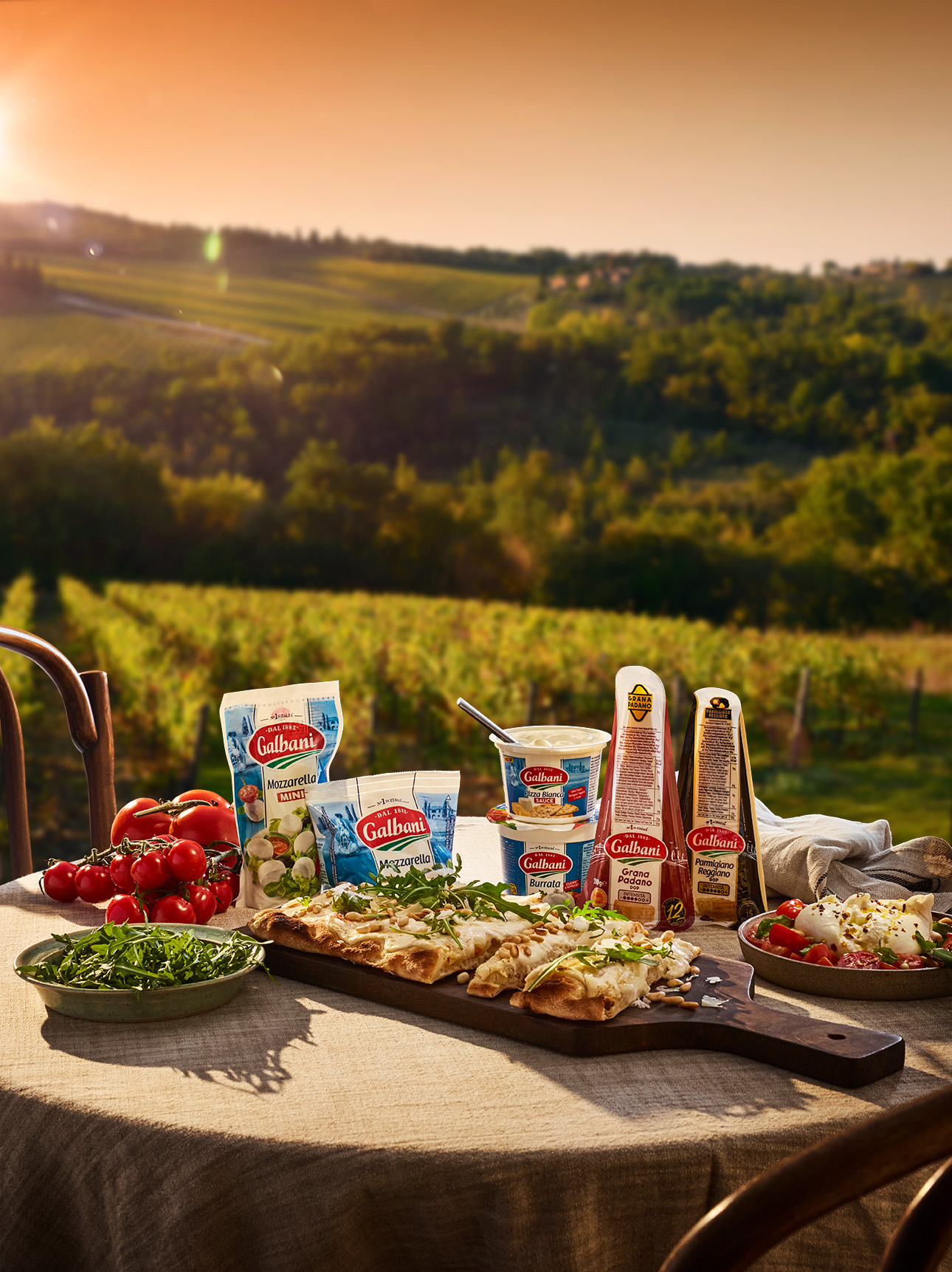 Italiensk sommarservering med Galbanis ostar, nybakad pizza och färska ingredienser framför ett soligt vinlandskap.